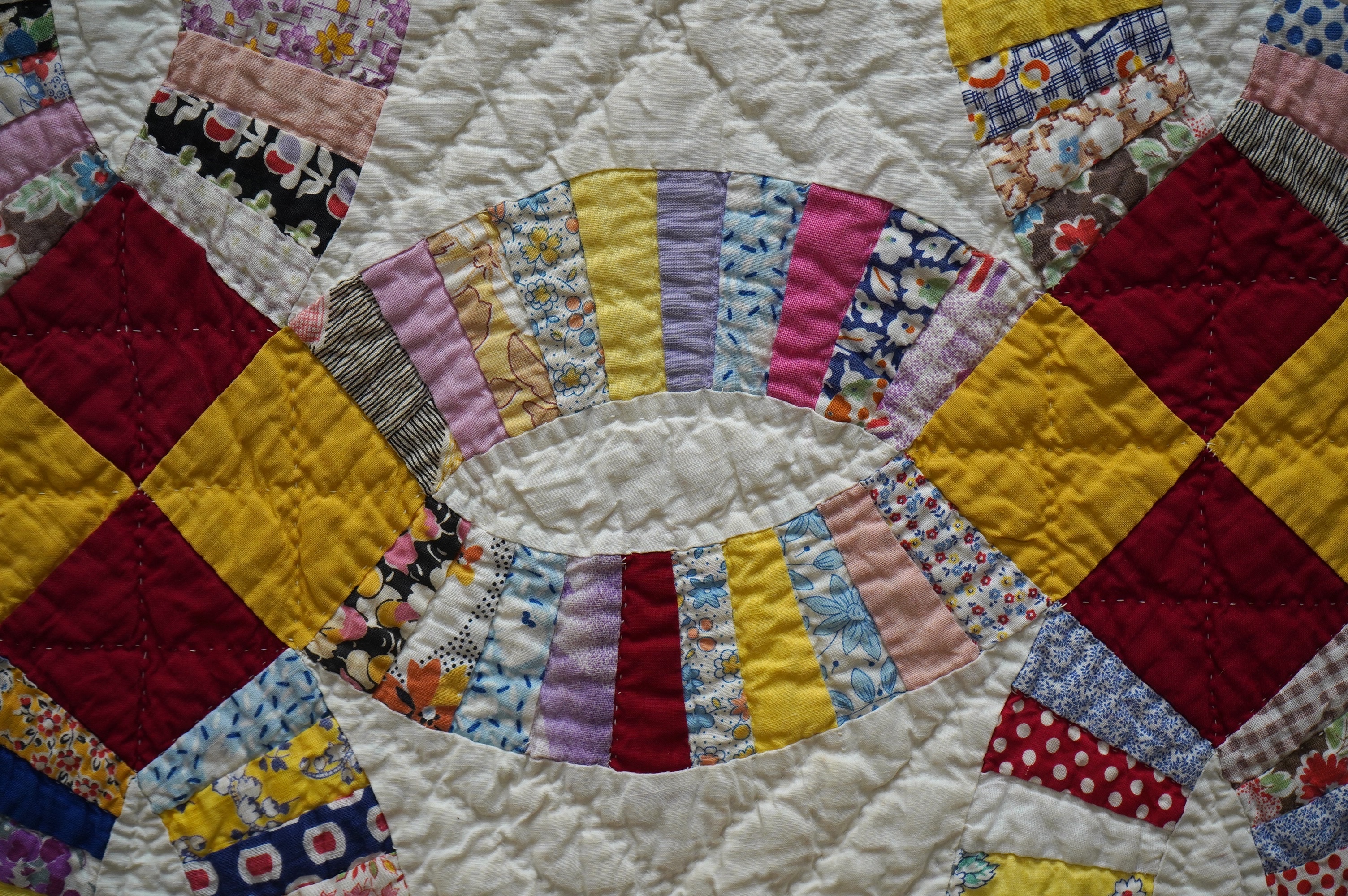 A 1940’s hand made ‘Double Wedding Ring’ patchwork quilt, made from bright multi-coloured floral and plain cotton dress fabrics into a patchwork design of large all over interlocking rings with a scalloped bright yellow